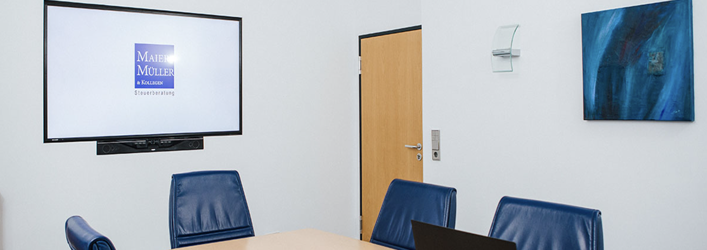 Moderne Konferenzraum mit Bildschirm, Tisch und blauen Stühlen, Wandschmuck und Tür im Hintergrund.