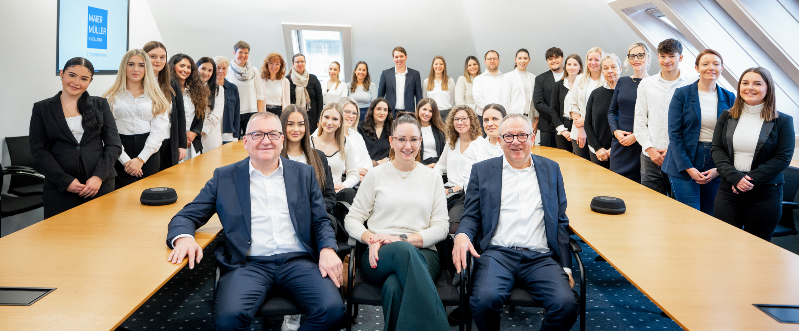 Eine Gruppe von Menschen in formeller Kleidung posiert gemeinsam in einem Besprechungsraum.